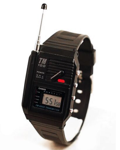 reloj digital hecho de resina de plástico negro. Tiene una pequeña pantalla con la hora en la parte de abajo, en la parte superior lleva un microfono y un botón, y en el lateral izquierdo tiene una pequeña antena extensible.